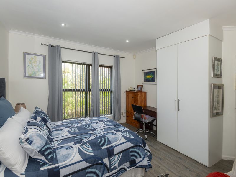 A well-maintained bedroom featuring built-in wardrobes, modern laminate flooring, recessed downlighting, and large windows with vertical blinds.