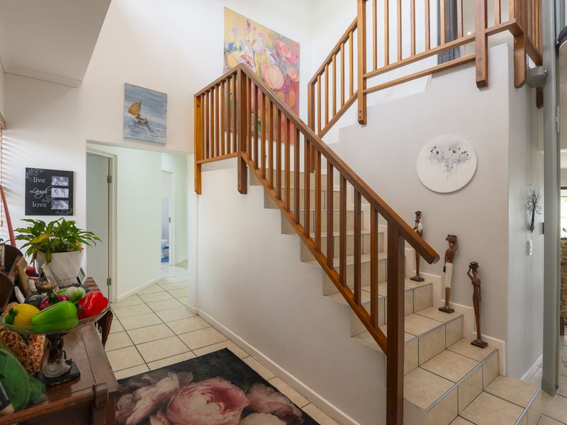 A bright entrance foyer featuring a timber staircase with matching balustrade and neutral tiled flooring, leading to an open-plan living area.