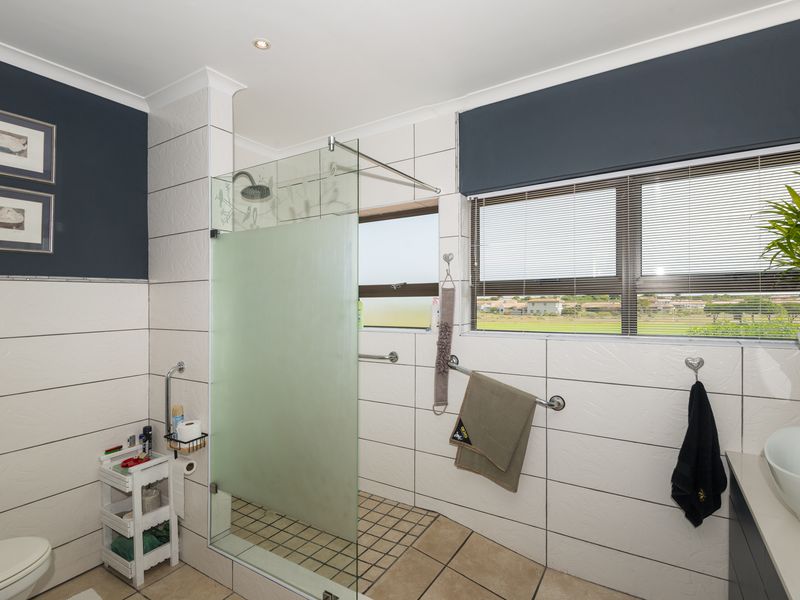 A well-maintained bathroom featuring a walk-in shower with a glass screen, tiled finishes, a modern vessel sink, and a window with blinds.
