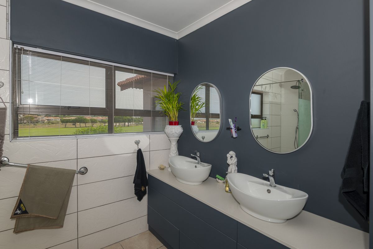 Modern bathroom featuring a double vanity with vessel sinks, chrome fixtures, tiled walls, and a separate shower enclosure with a view.