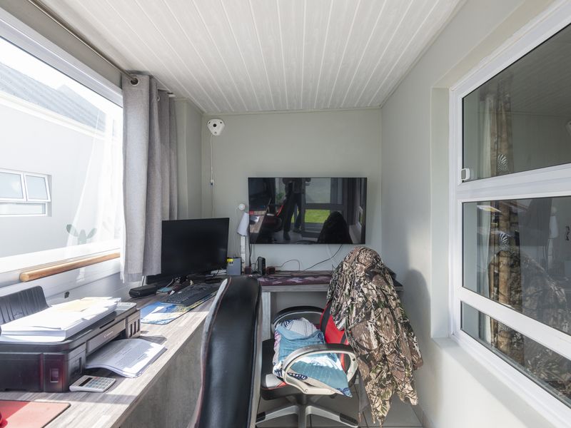 A compact home office space featuring tiled flooring, tongue and groove ceiling, and large windows providing natural light.