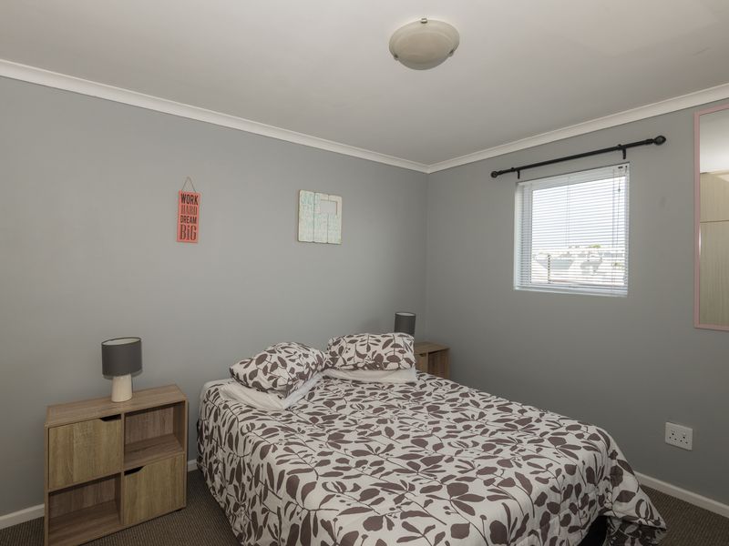 A functional bedroom featuring neutral grey walls, a window with blinds, and a ceiling-mounted light fixture.