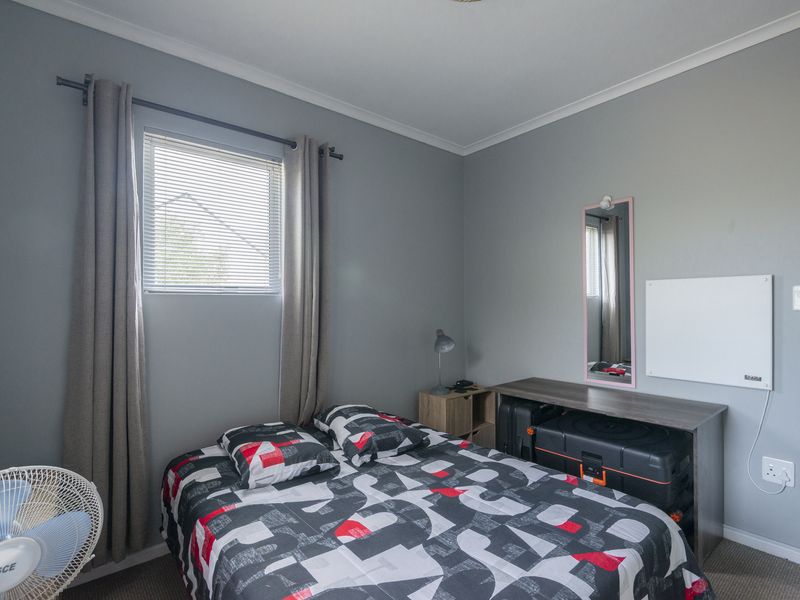 A functional bedroom featuring grey walls, carpeted flooring, and a window with venetian blinds.