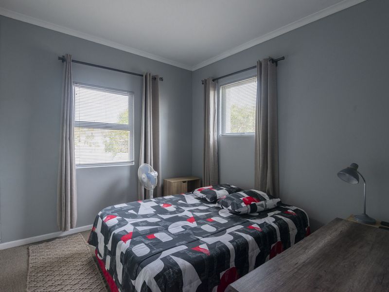 A functional bedroom featuring built-in cupboards, neutral grey walls, and natural light through aluminium-framed windows.