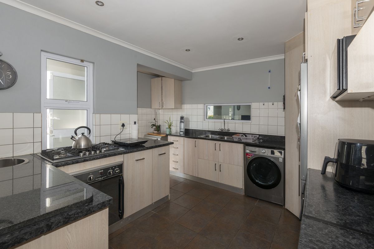 A functional kitchen featuring granite countertops, light wood cabinetry, a gas hob, built-in oven, and integrated laundry plumbing.