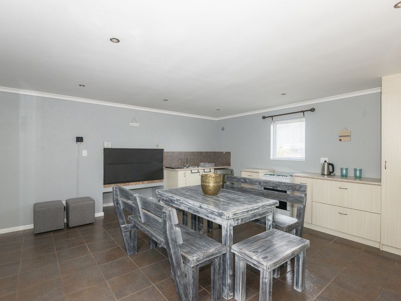Open-plan living area featuring a built-in braai, tiled flooring, and functional kitchen cabinetry with integrated storage.