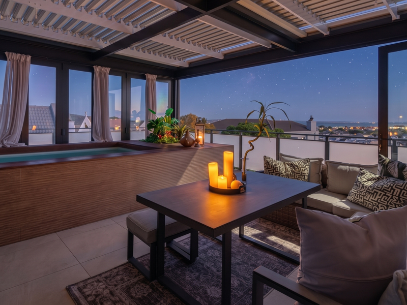 A modern covered balcony featuring a built-in plunge pool, louvered roof, and expansive bi-fold doors offering panoramic evening views.