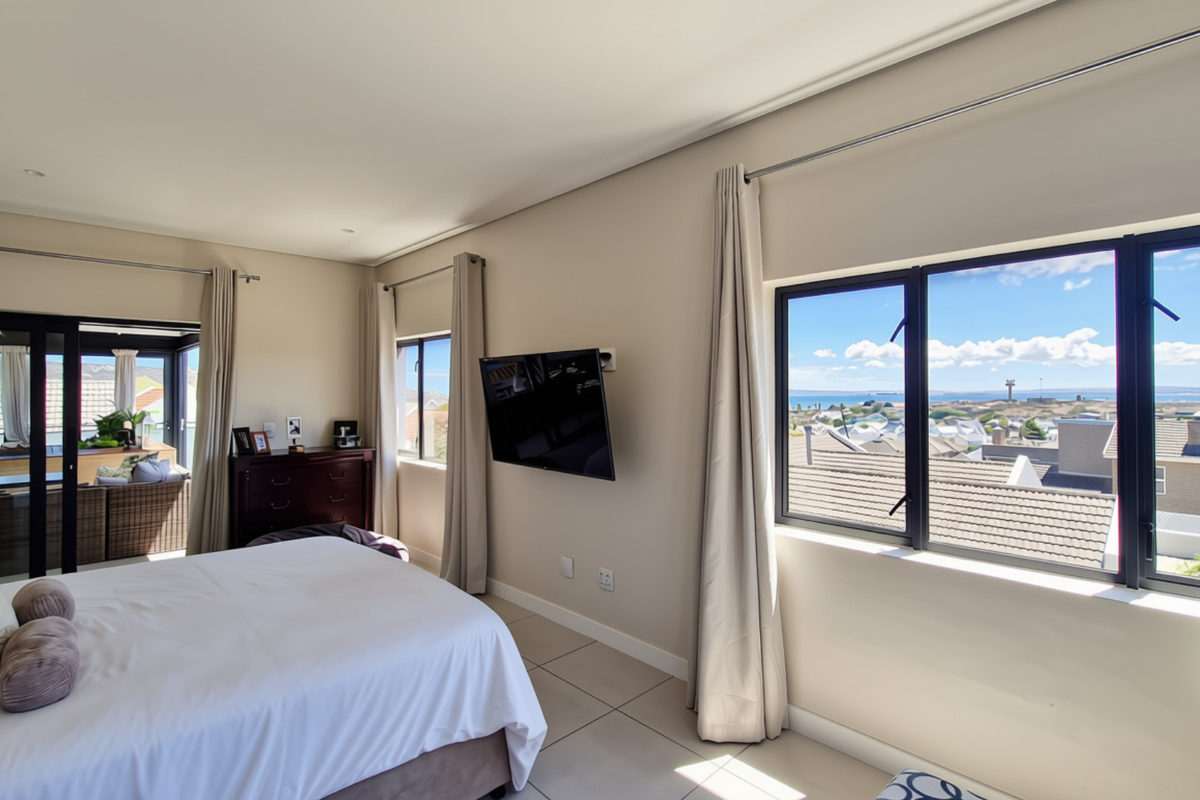 Spacious bedroom featuring tiled flooring, large windows with coastal views, and sliding glass doors leading to an outdoor patio area.