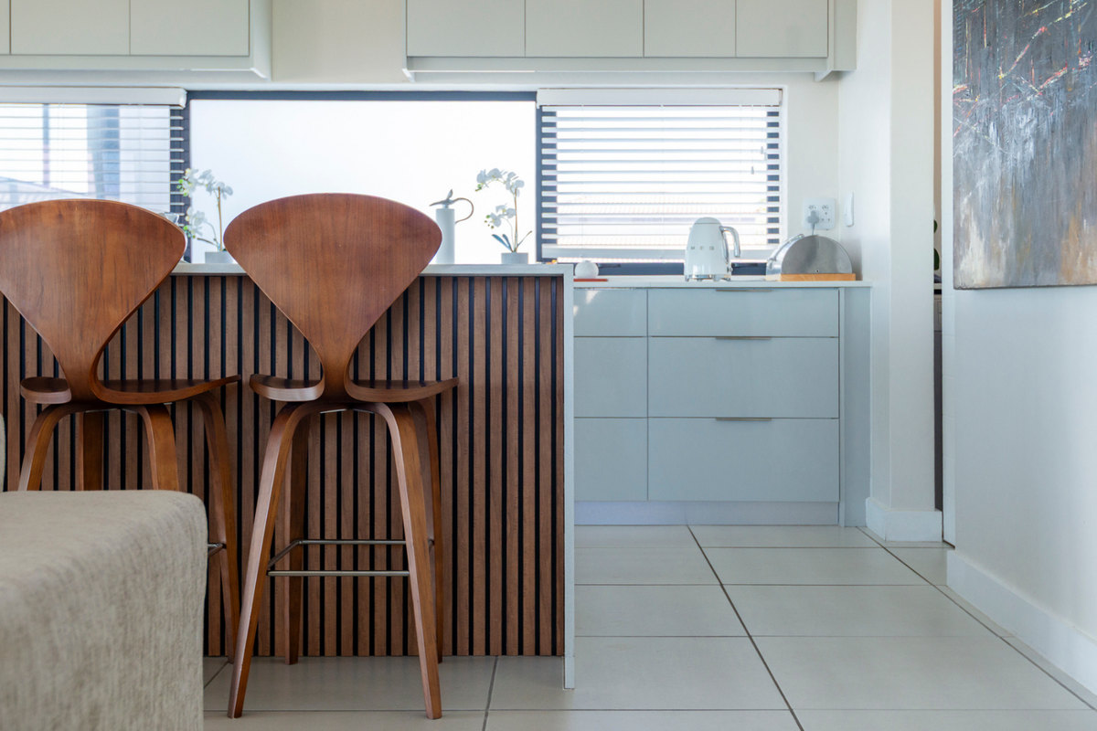 Modern kitchen featuring a stylish slatted timber island, handleless cabinetry, and neutral tiled flooring in a bright, well-maintained space.