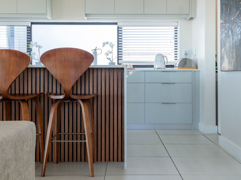 Modern kitchen featuring a stylish slatted timber island, handleless cabinetry, and neutral tiled flooring in a bright, well-maintained space.