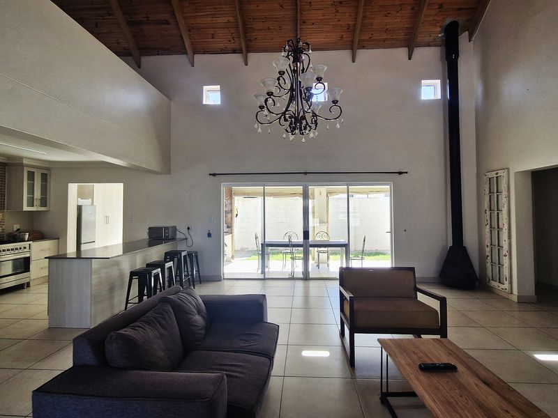 Spacious open-plan living area featuring a vaulted timber ceiling, a modern freestanding fireplace, and a well-appointed kitchen with a central island and gas hob.