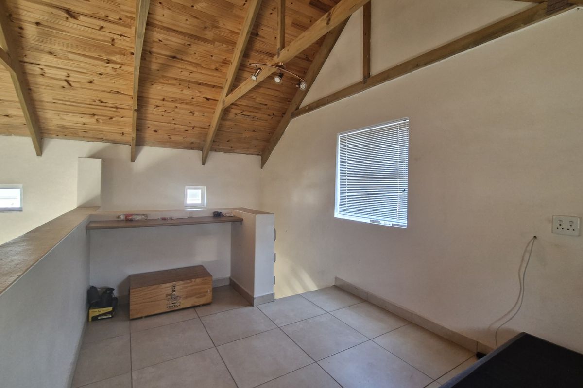 An open-plan loft area featuring exposed timber vaulted ceilings, tiled flooring, and built-in shelving, offering a versatile space with natural light.