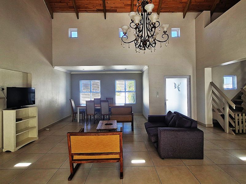 Spacious open-plan living and dining area featuring high exposed timber ceilings, tiled flooring, and a grand chandelier, with an adjoining staircase.