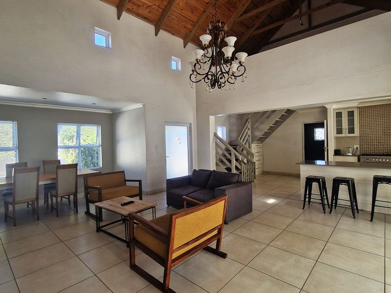 Spacious open-plan living area featuring high vaulted ceilings with exposed timber rafters, tiled flooring, and a functional kitchen with a breakfast bar.
