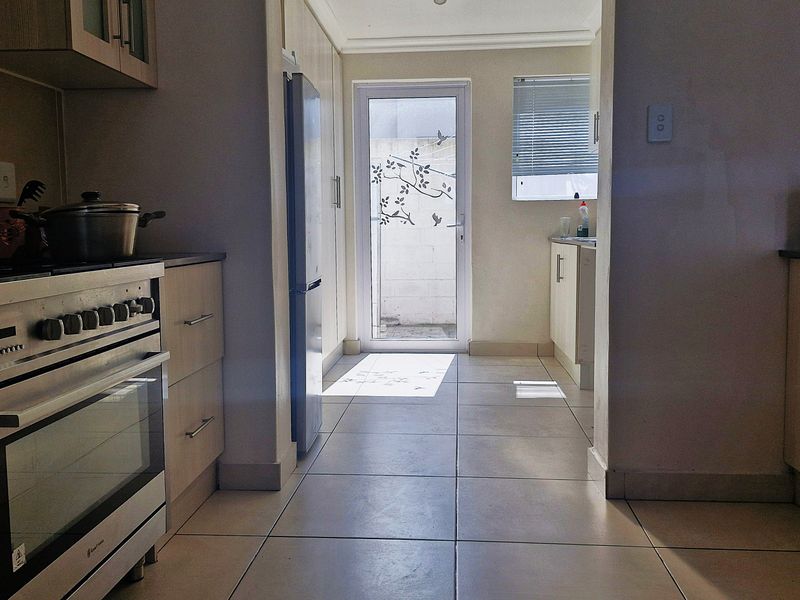 A functional kitchen featuring light wood cabinetry, tiled flooring, a gas stove with oven, and direct access to an outdoor area through a glass door.