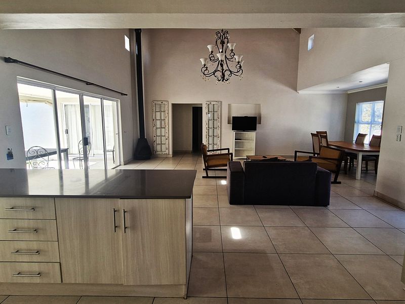 Spacious open-plan living area featuring a modern kitchen island, tiled flooring, a high ceiling with a fireplace, and seamless access to the outdoor patio.