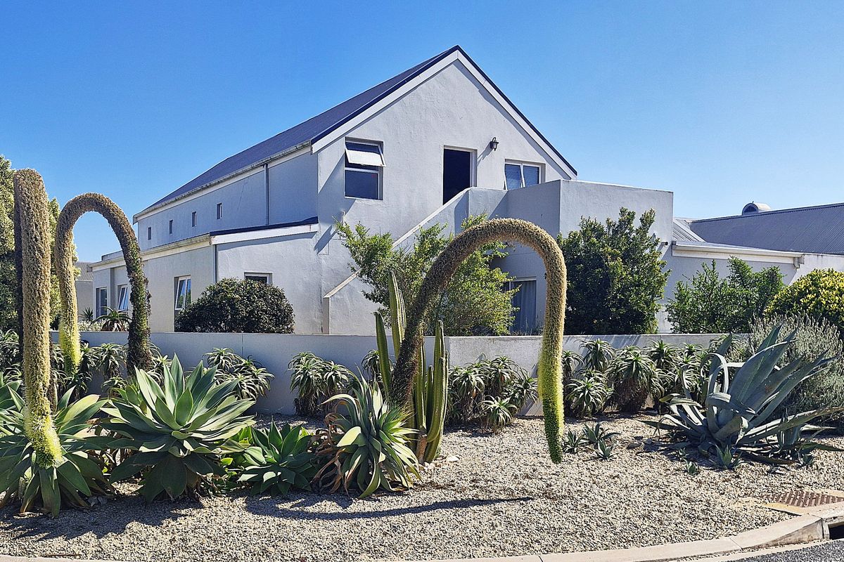 Rear view of a multi-level residential property featuring a pitched roof, external staircase, and established garden with drought-tolerant landscaping.