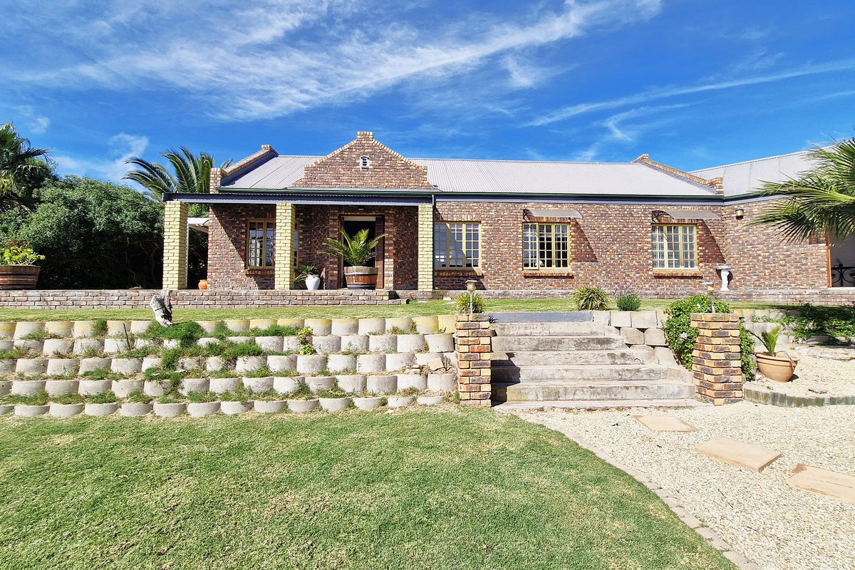A rear view of a face brick house featuring a covered patio, concrete staircase, and tiered retaining wall garden.