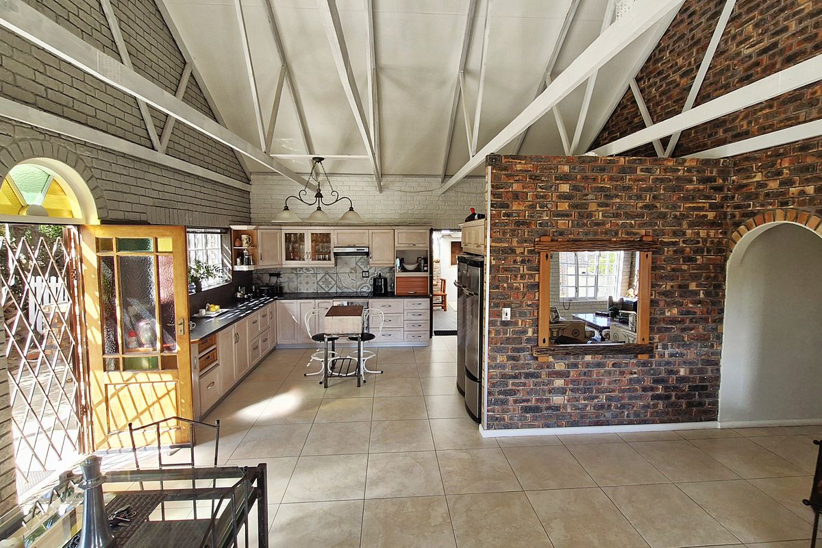 Spacious kitchen featuring exposed roof trusses, brick feature walls, tiled flooring, and ample built-in cabinetry with a functional layout.