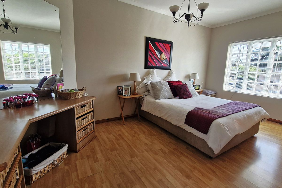Spacious bedroom featuring light laminate flooring, a built-in vanity with a large mirror, and dual windows with blinds providing ample natural light.
