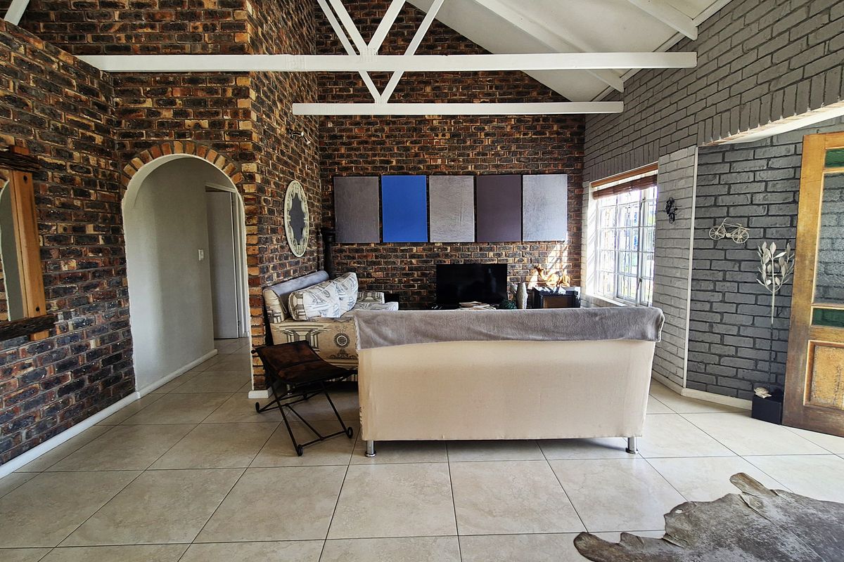 Spacious living room featuring exposed brick walls, vaulted ceilings with exposed trusses, and large format floor tiles, creating a rustic and character-filled atmosphere.
