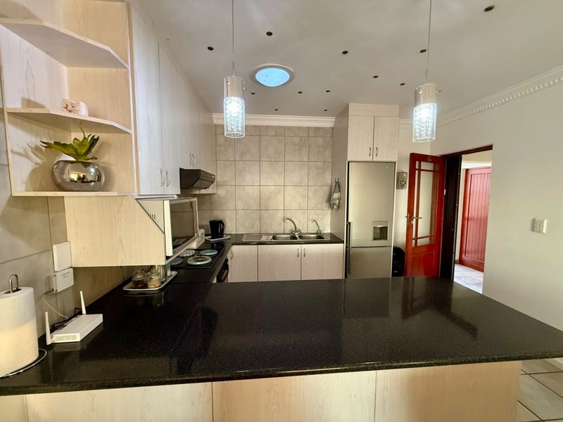A well-lit kitchen featuring light wood cabinetry, dark granite countertops, a tiled backsplash, and a functional layout with integrated appliances and a skylight.