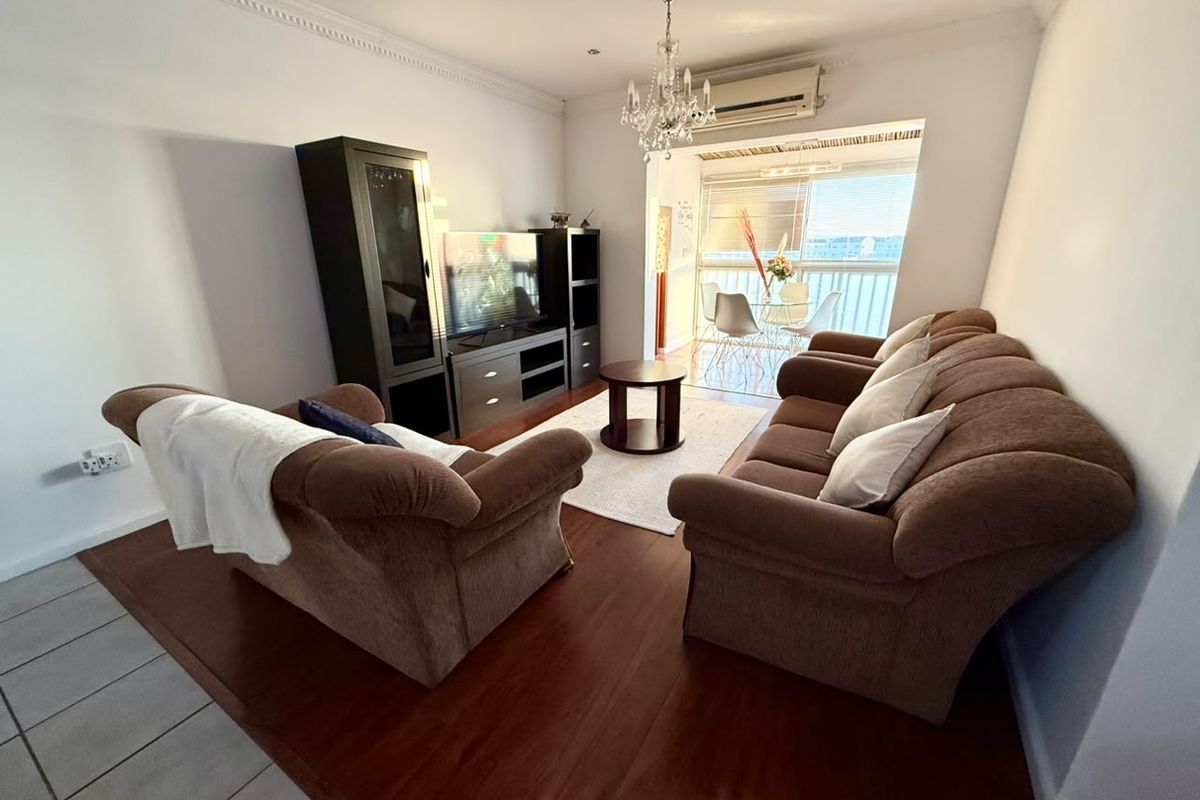 A well-maintained living room featuring laminate flooring, crown molding, and a split-system air conditioner, with direct access to a balcony area.