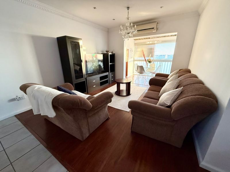 A well-maintained living room featuring laminate flooring, crown molding, and a split-system air conditioner, with direct access to a balcony area.