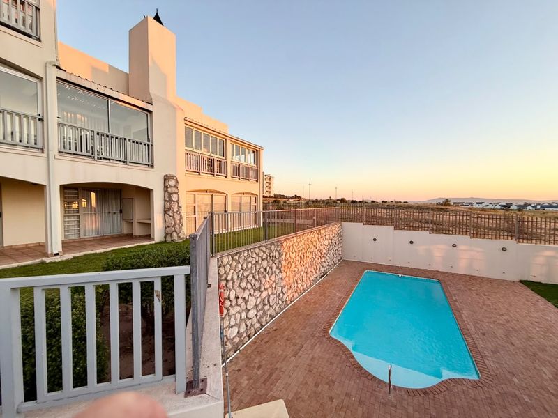 Exterior view of an apartment complex featuring a private swimming pool, stone retaining wall, brick paved patio, and upper-level balconies.