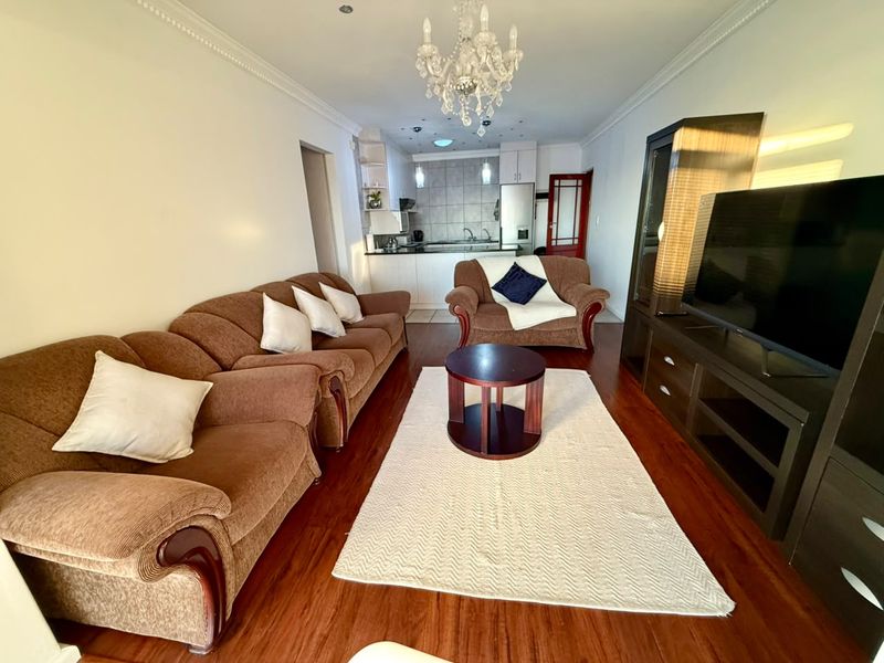 Open-plan living area featuring laminate flooring, crown molding, and a connected kitchen with tiled backsplash and cabinetry.