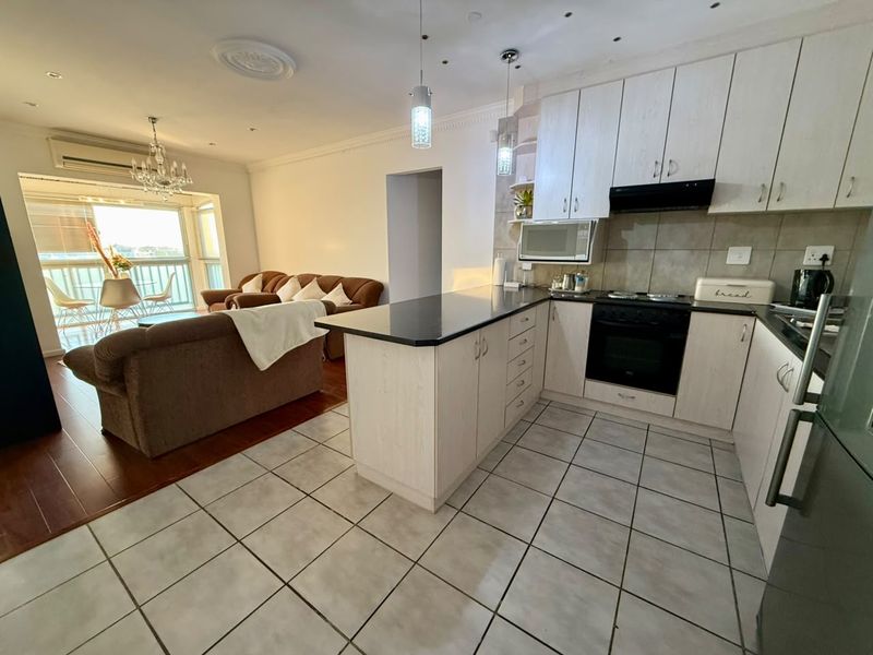 Open-plan living area featuring a modern kitchen with built-in appliances, granite countertops, and seamless transition to a balcony with natural light.