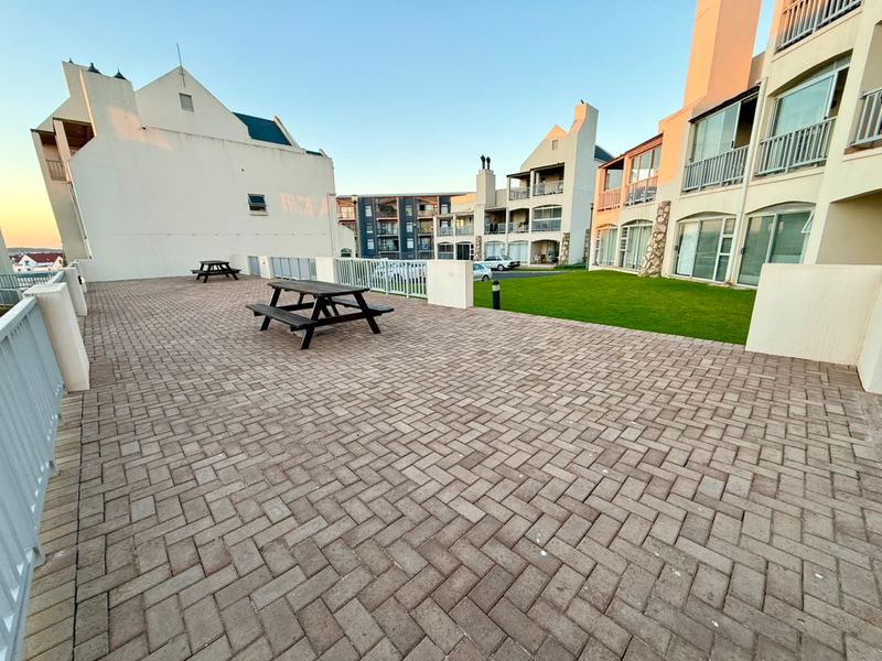 A spacious paved communal patio area with a well-maintained lawn, surrounded by apartment building facades.
