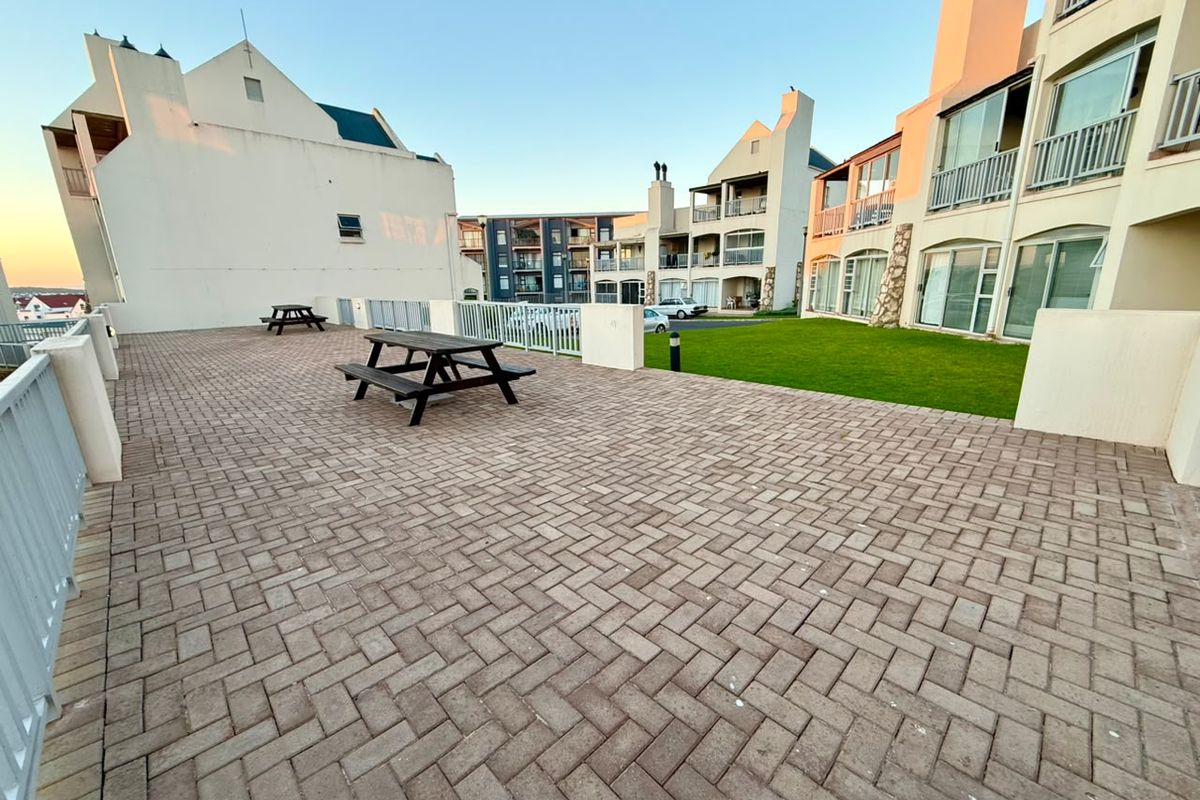 A spacious paved communal patio area with a well-maintained lawn, surrounded by apartment building facades.