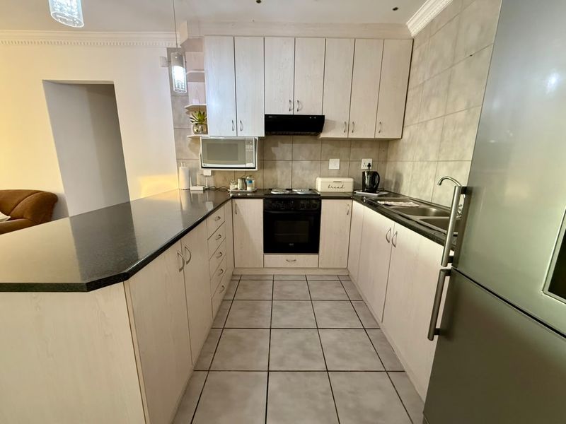 A functional kitchen featuring light wood-finish cabinetry, dark granite countertops, built-in oven with hob, extractor fan, and tiled flooring.