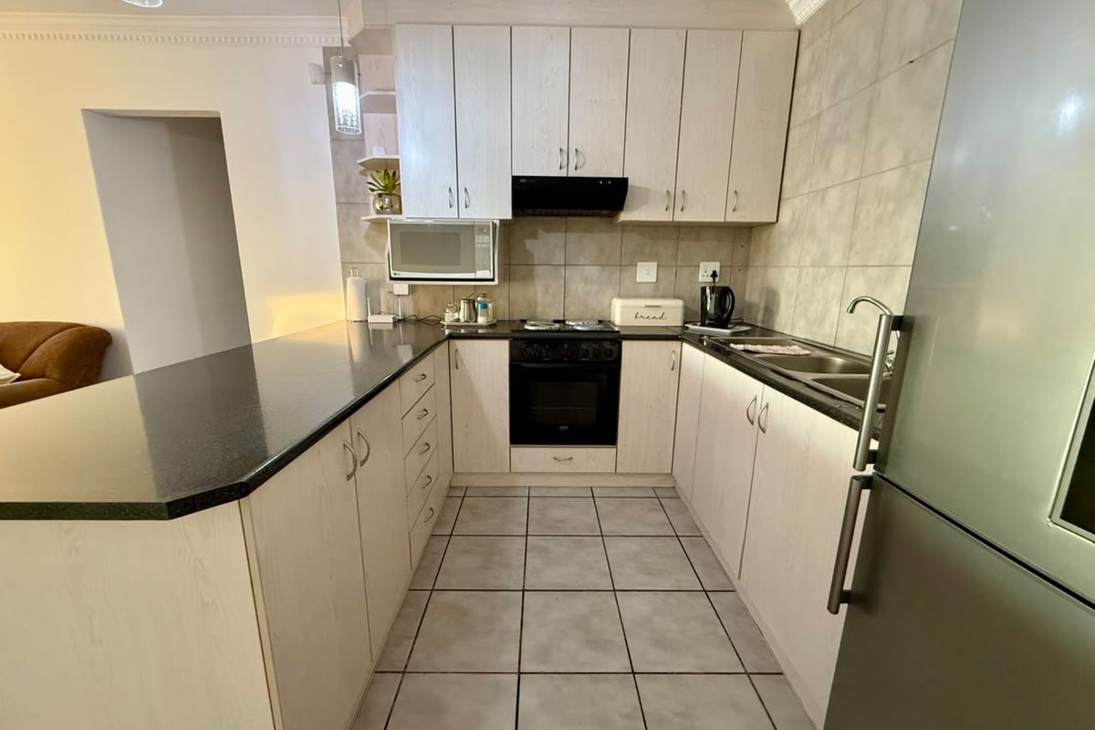 A functional kitchen featuring light wood-finish cabinetry, dark granite countertops, built-in oven with hob, extractor fan, and tiled flooring.