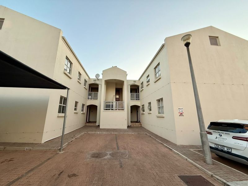 Exterior view of an apartment complex featuring a paved driveway, multiple balconies, and a central entrance area.
