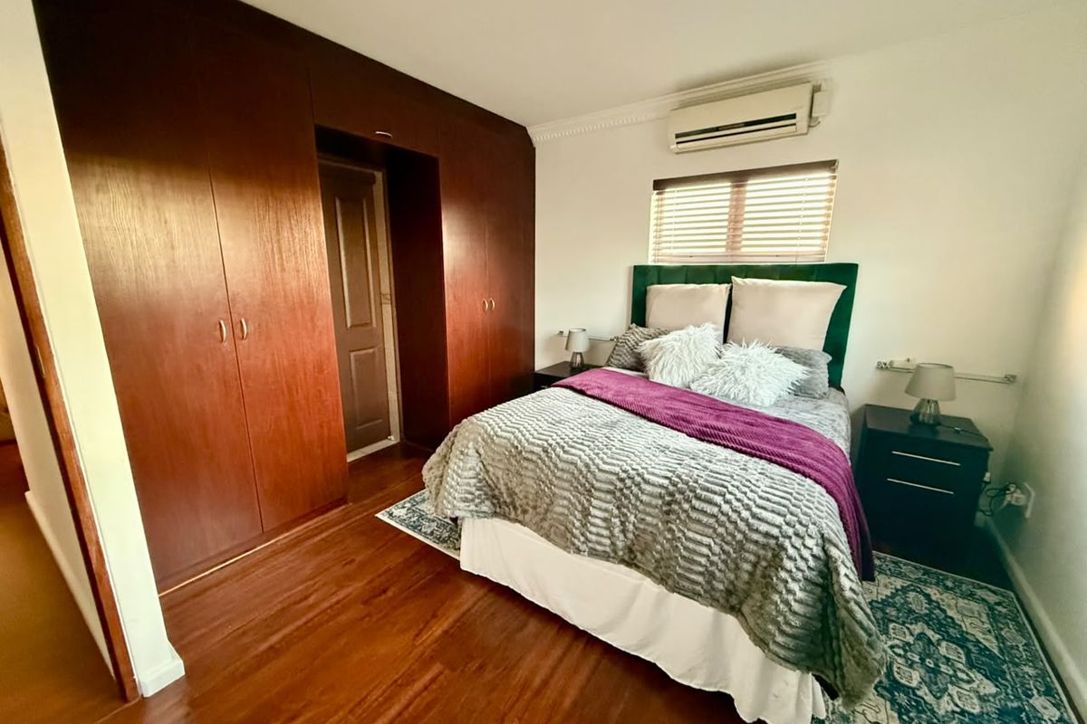 A well-maintained bedroom featuring warm-toned laminate flooring, extensive built-in wooden cabinetry, and a wall-mounted air conditioning unit.