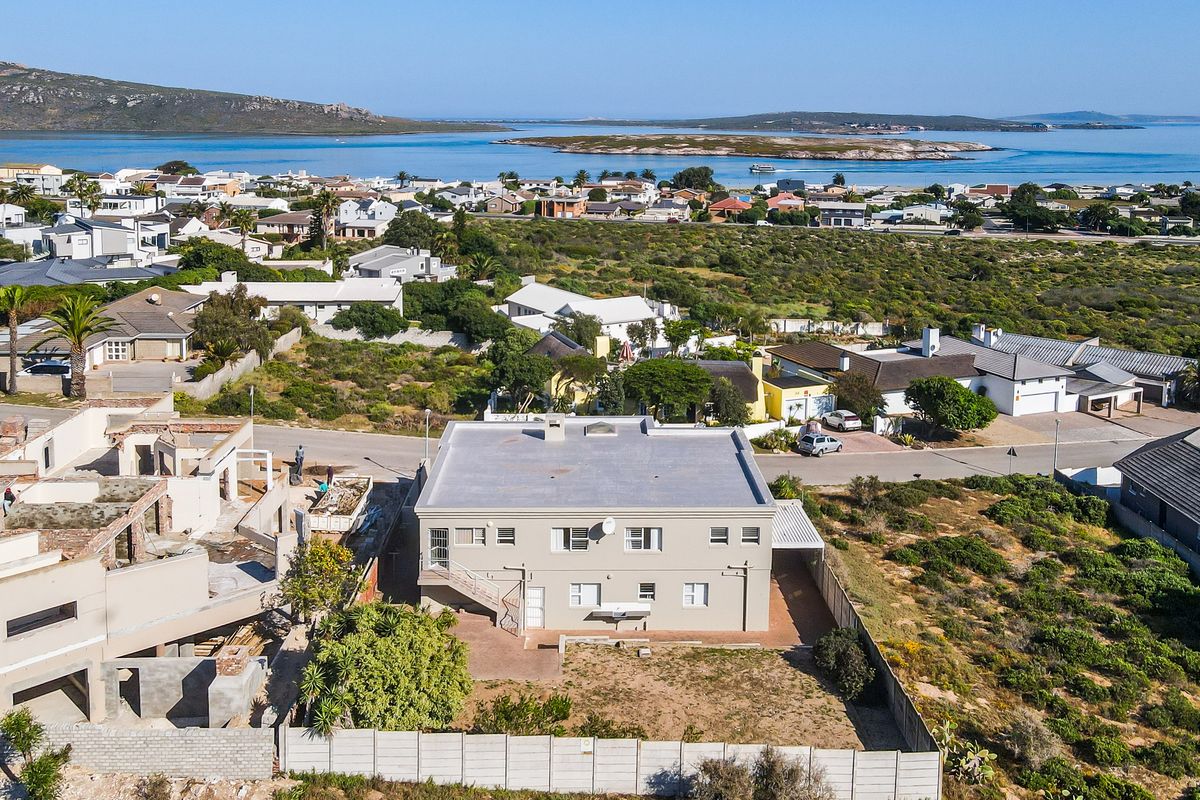 Aerial view of a residential property featuring a flat roof, paved patio, and boundary wall, situated in a coastal neighborhood with scenic water views.