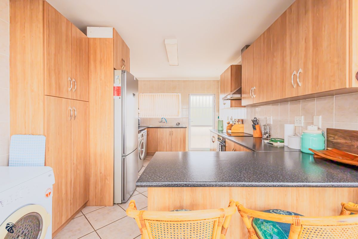 Functional kitchen featuring light wood-look cabinetry, dark laminate countertops, tiled backsplash, and integrated laundry plumbing, offering a practical layout for daily use.