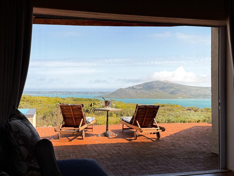 A covered patio featuring brick paving and expansive views of the lagoon and surrounding landscape, accessible through a large sliding door.