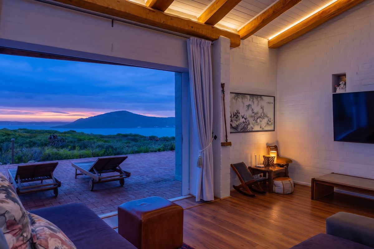 A beautifully appointed living room featuring exposed timber beams, recessed lighting, and seamless indoor-outdoor flow to a patio with stunning coastal and mountain views.