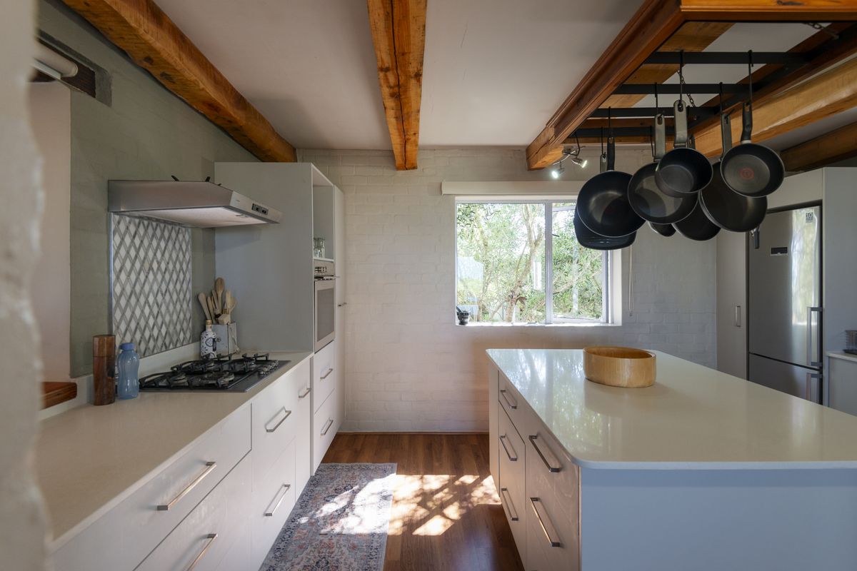 Modern kitchen featuring a central island, gas hob, built-in oven, and exposed timber ceiling beams, creating a warm and functional culinary space.