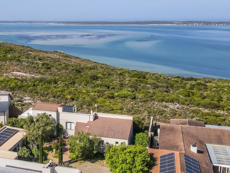 Aerial view of a coastal residential property featuring solar panels, tiled roofing, and proximity to the lagoon and natural landscape.