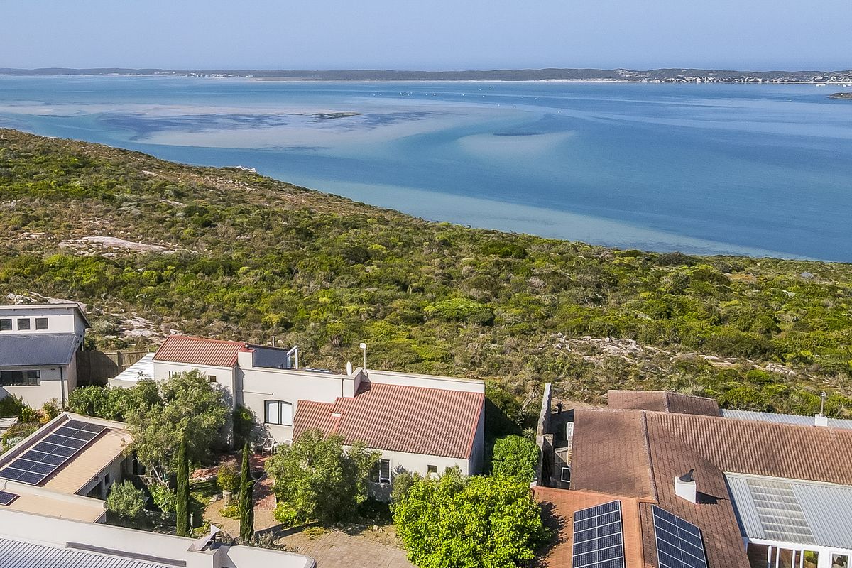 Aerial view of a coastal residential property featuring solar panels, tiled roofing, and proximity to the lagoon and natural landscape.
