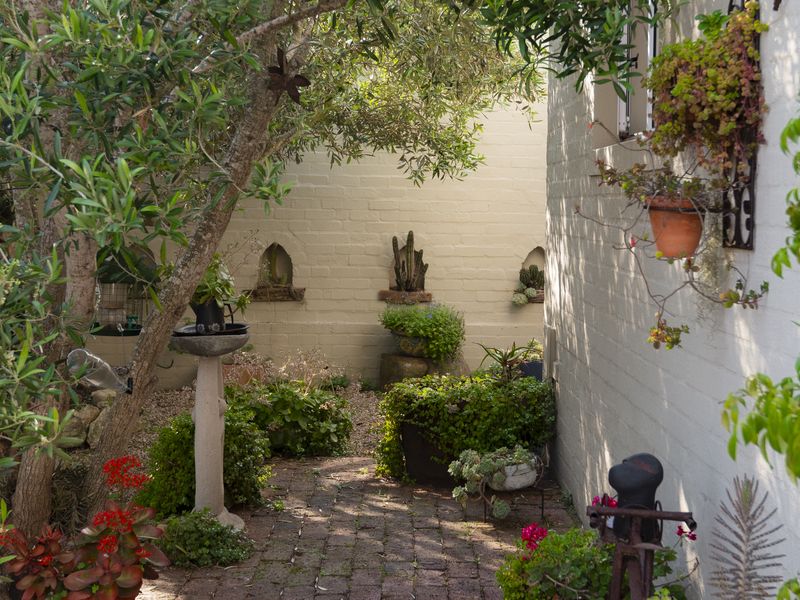 A charming, landscaped garden area featuring brick paving, mature trees, and decorative wall niches set against a painted masonry wall.