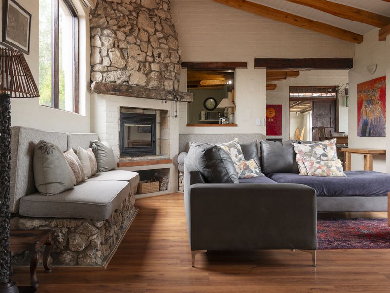 A cozy living room featuring a prominent stone fireplace, exposed timber ceiling beams, and warm laminate flooring with built-in stone bench seating.