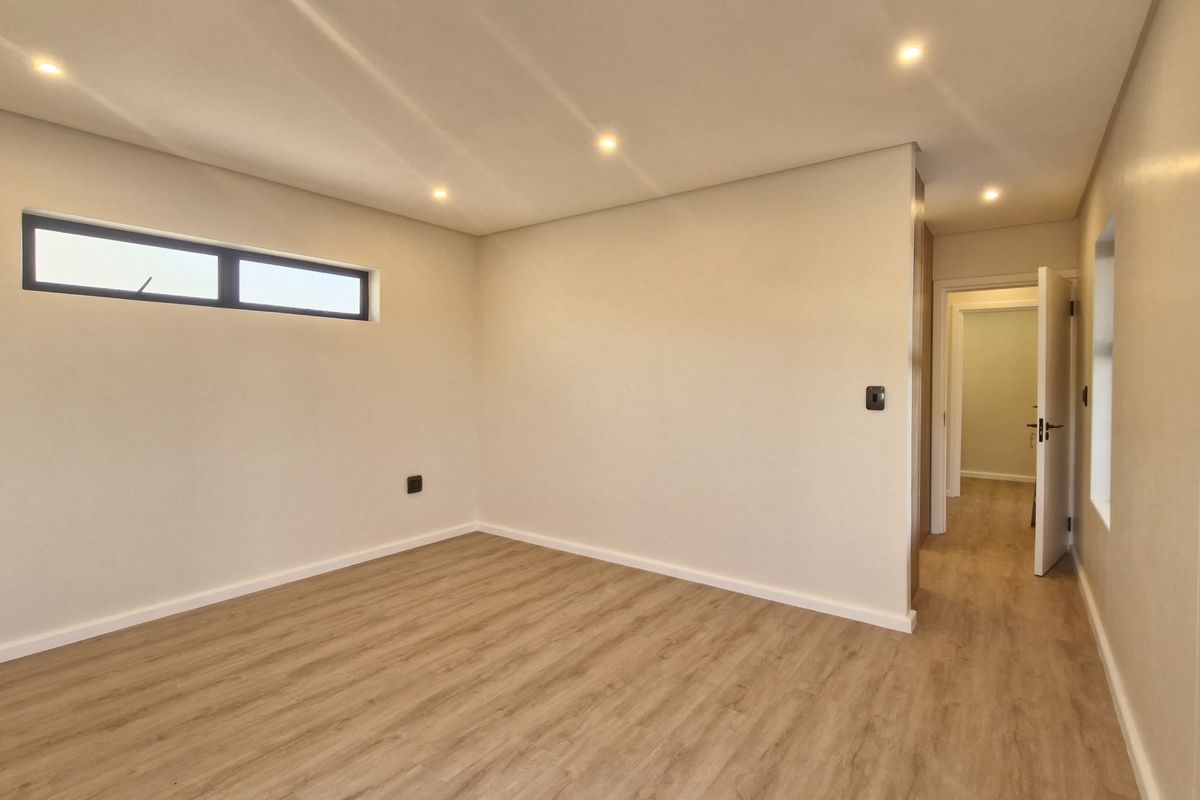 A bright, empty bedroom featuring modern laminate flooring, recessed downlighting, and a horizontal clerestory window, providing a clean and neutral canvas.