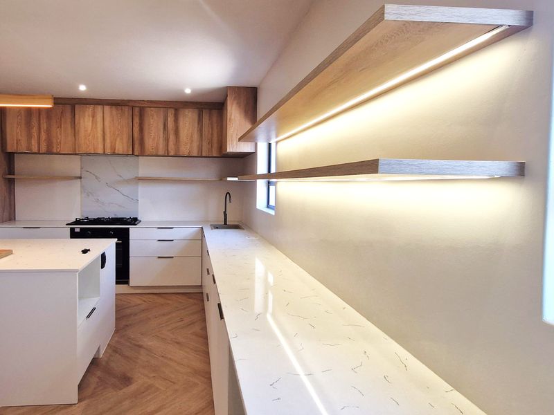 Modern kitchen featuring sleek white cabinetry, stone countertops, herringbone flooring, and integrated LED lighting on floating shelves.