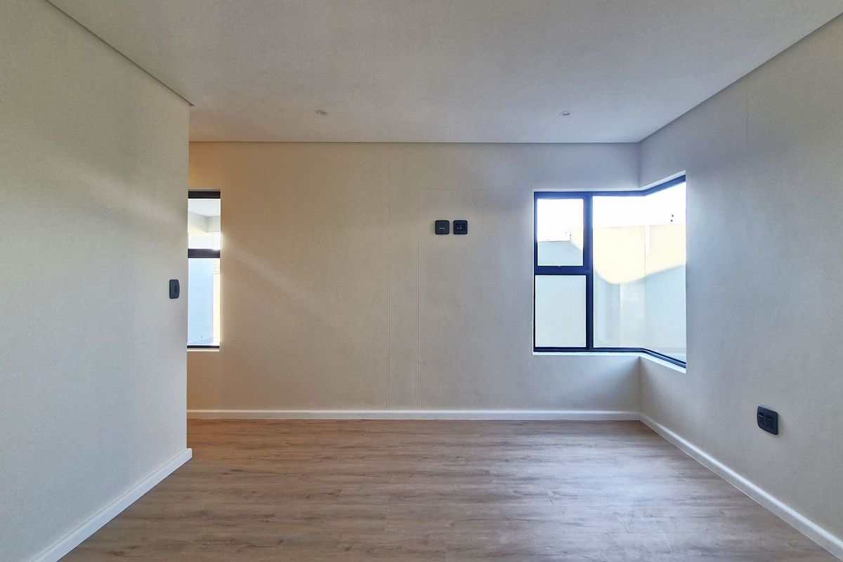 A bright, empty living area featuring modern laminate flooring, neutral walls, and large aluminium-framed windows providing ample natural light.