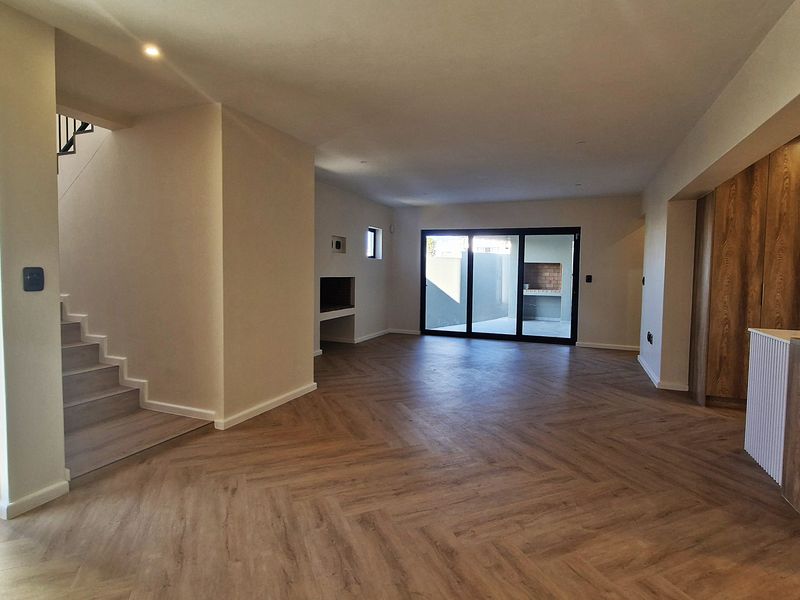 Spacious open-plan living area featuring modern herringbone flooring, recessed lighting, a built-in fireplace, and a sleek kitchen with integrated cabinetry.